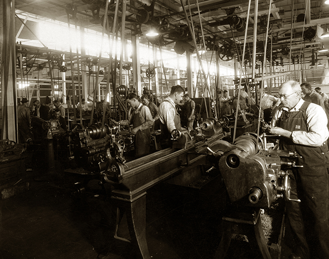 Uma antiga foto em preto e branco de uma antiga fábrica e seus trabalhadores.