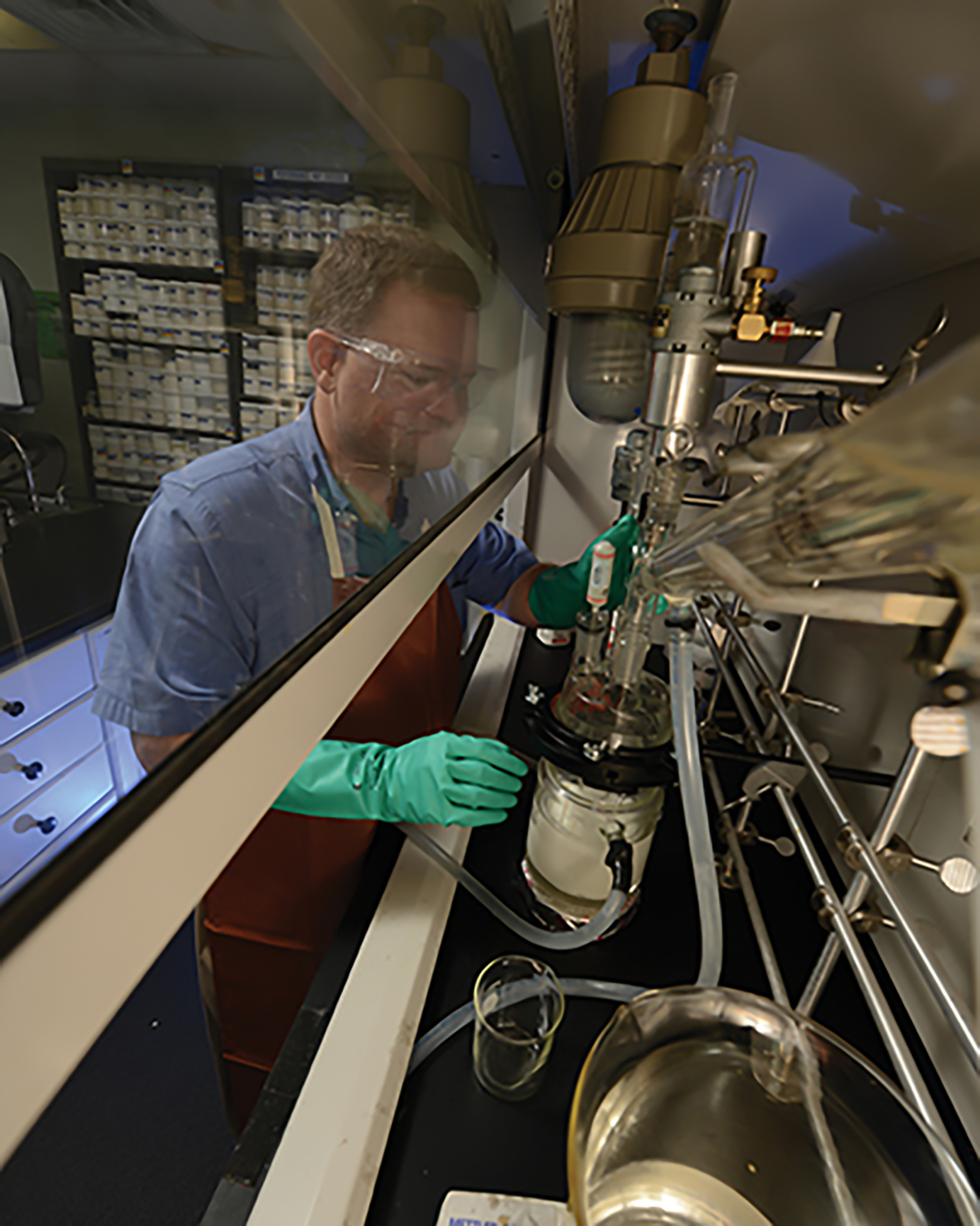 Man wearing protective glasses and gloves operating chemistry equipment.