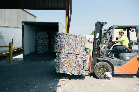 Empilhadeira transportando fardos de latas de alumínio